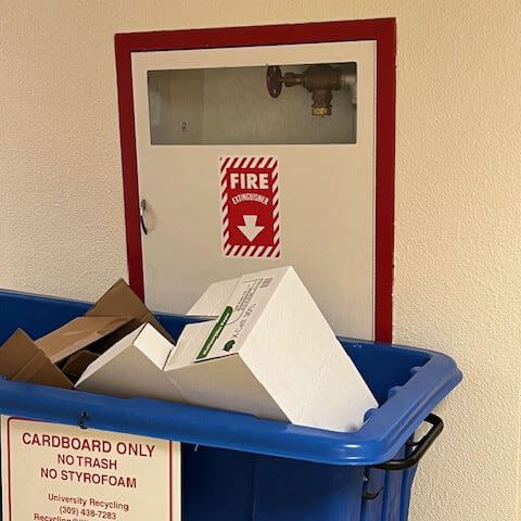 A fire extinguisher blocked by a recycling bin.