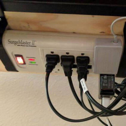 A power strip secured to the bottom of a desk.