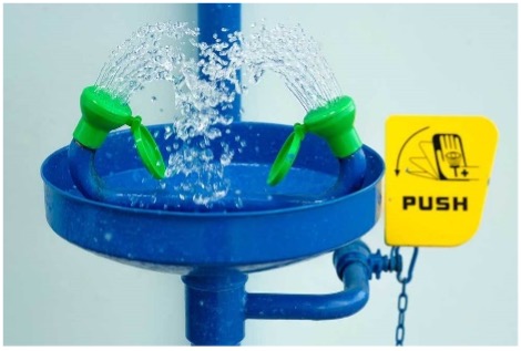 Blue eyewash station with spraying nozzles and a yellow push sign.